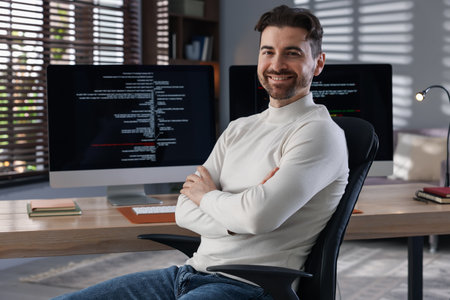 Portrait of smiling programmer with crossed arms on chair at workplace