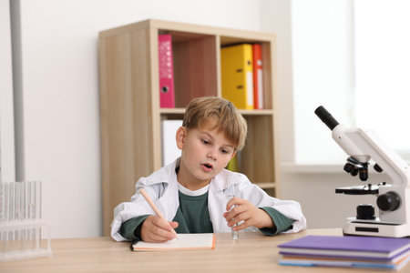 Cute little boy with test tube and microscope writing at desk indoors. Child and scienceの写真素材