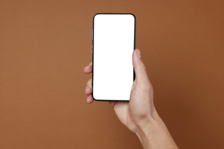 Person holding smartphone with blank screen on brown background, closeup. Mockup for designの写真素材