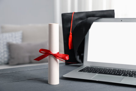 Diploma, graduation hat and laptop on gray wooden table indoors, selective focusの写真素材