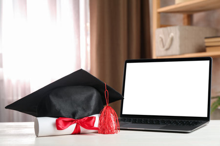 Diploma, graduation cap and laptop on white wooden table indoors, closeupの写真素材