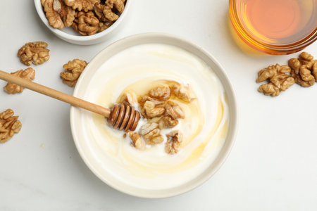 Delicious Greek yogurt with honey and nuts on white table, flat layの写真素材