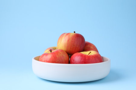 Ripe red apples in bowl on light blue background, closeupの写真素材