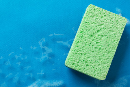 Kitchen sponge and foam on light blue background, top view. Space for text