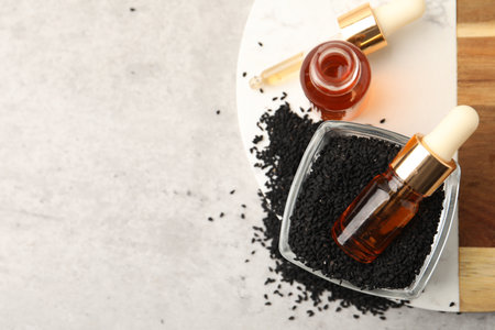 Black cumin seeds and oil on light gray table, flat lay. Space for textの写真素材