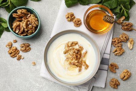 Delicious Greek yogurt with honey, nuts and mint on light gray table, flat layの写真素材