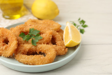 Deep fried squid rings with parsley and lemon slice on white table, closeupの写真素材