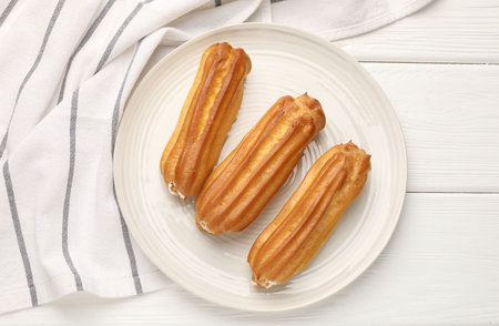 Fresh tasty eclairs on white wooden table, top view
