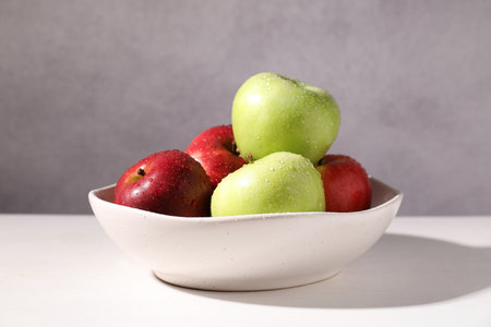Fresh red and green apples with water drops in bowl on white table against gray background, closeupの写真素材