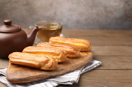 Tasty eclairs and tea on wooden table. Space for textの写真素材