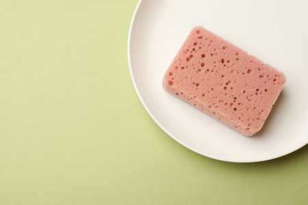 Kitchen sponge and plate on light green background, top view. Space for textの写真素材