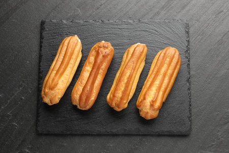 Tasty eclairs on black table, top view
