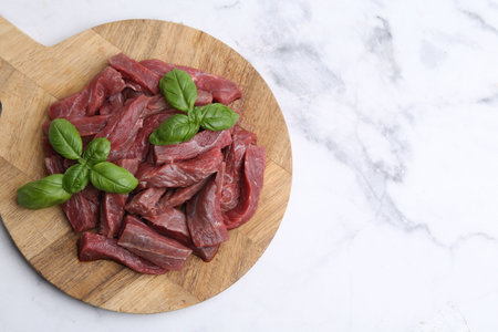 Pieces of raw beef meat and basil on white marble table, top view. Space for textの写真素材