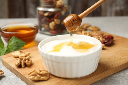 Dripping honey into Greek yogurt and walnuts on gray table, closeupの写真素材
