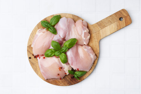 Raw chicken thighs with basil on white tiled table, top viewの写真素材