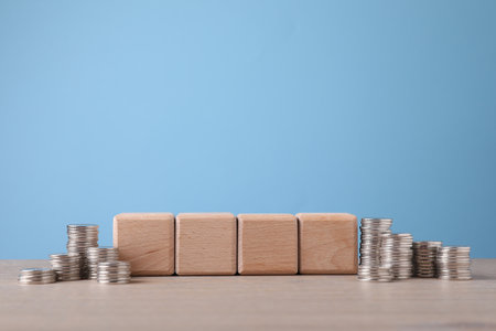 Empty cubes and stacked coins on table against light blue background. Space for designの写真素材