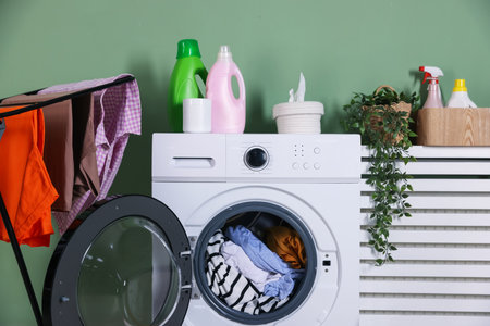 Modern washing machine, detergents, houseplant and clothes near light green wall indoorsの写真素材