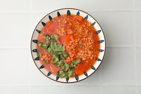Tasty lentil soup in bowl on white tiled table, top viewの写真素材