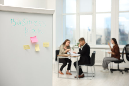 Colleagues discussing strategy in office, focus on whiteboard with text Business Plan and sticky notesの写真素材