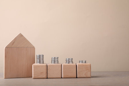 Empty cubes with stacked coins and figure of house on wooden table against beige background. Space for designの写真素材