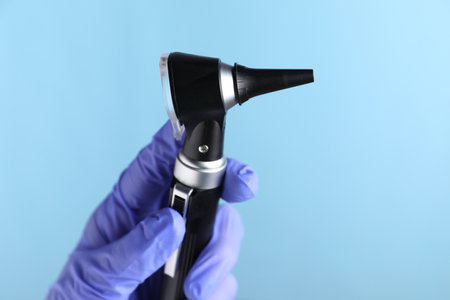 Doctor with otoscope on light blue background, closeupの写真素材