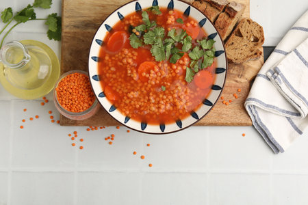 Tasty lentil soup in bowl served on white tiled table, flat lay. Space for textの写真素材