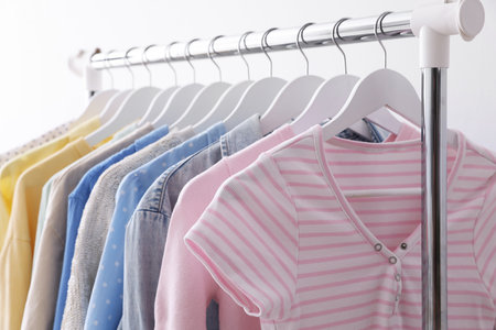 Different stylish clothes hanging on rack near white wall indoors, closeup