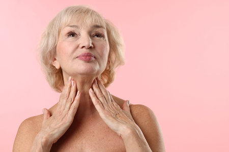 Senior woman touching her neck on light pink background. Space for textの写真素材