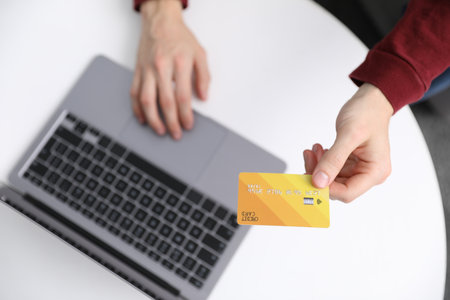 Young man making online payment with laptop and credit card at white table indoors, top viewの写真素材