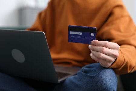 Young man making online payment with laptop and credit card indoors, closeupの写真素材