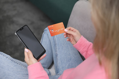 Woman making online payment with phone and credit card indoors, closeupの写真素材