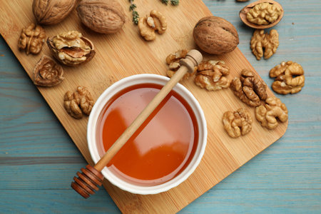 Honey in bowl, walnuts and dipper on light blue wooden table, flat lay