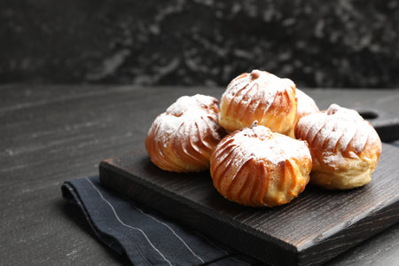 Tasty profiteroles with powdered sugar on black table, closeup. Space for text