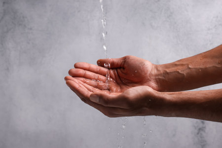 Pouring water into hands against light gray background, closeup. Space for text