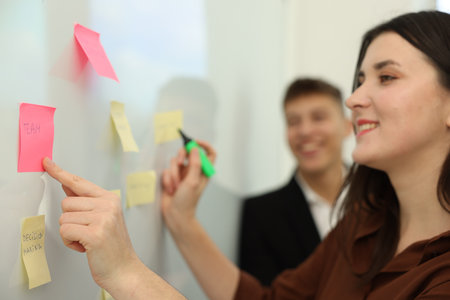 Colleagues discussing strategy near whiteboard with sticky notes in office, selective focus