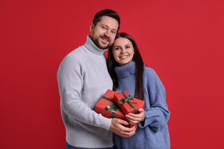 Happy couple with Christmas gifts on red backgroundの写真素材