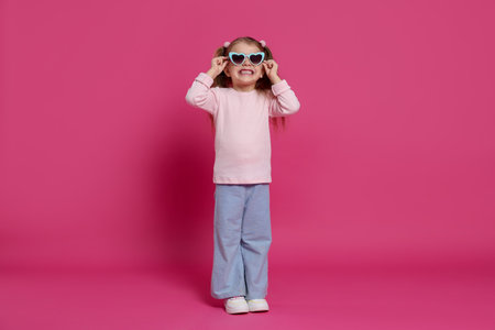 Smiling little girl in sunglasses on pink backgroundの写真素材