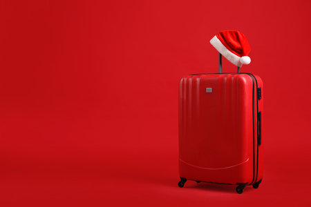 Christmas vacation. Suitcase with Santa hat on red background, space for textの写真素材