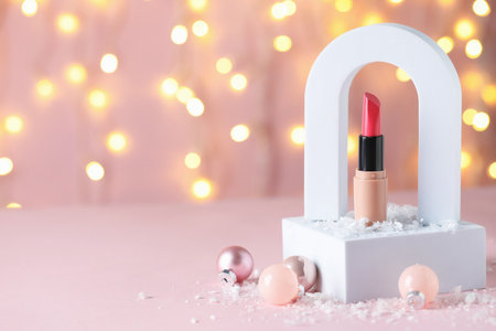 Stylish presentation of lipstick and Christmas baubles on pink table against blurred lights, closeup. Space for textの写真素材