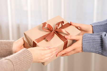 Merry Christmas and Happy New Year. Woman giving gift box to her friend indoors, closeup