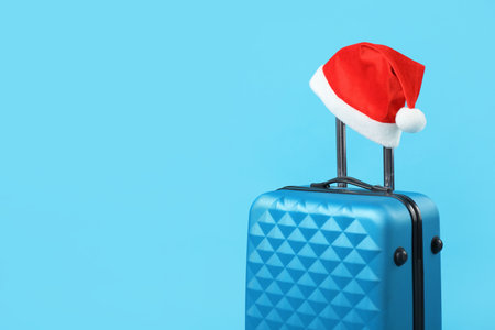 Christmas vacation. Suitcase with red Santa hat on light blue background. Space for textの写真素材