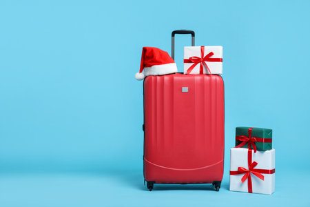 Christmas vacation. Red suitcase, Santa hat and gift boxes on light blue background. Space for textの写真素材