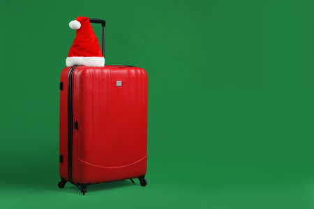 Santa hat on red suitcase against green background, space for text. Christmas vacationの写真素材