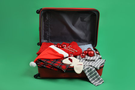 Christmas vacation. Open suitcase with Santa hat, clothes, baubles and candy canes on green backgroundの写真素材