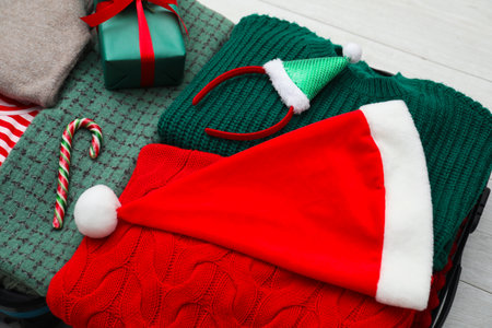 Christmas vacation. Suitcase with Santa hat, gift box and candy cane on floor indoors, closeupの写真素材