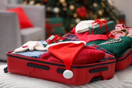 Christmas vacation. Suitcase with Santa hat, clothes, gift boxes and candy canes indoors, closeupの写真素材