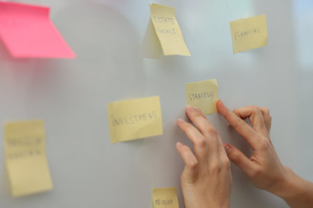 Woman sticking note with word Strategy on whiteboard in office, closeupの写真素材