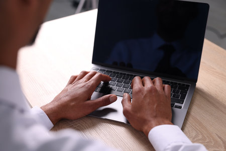 African-American man using laptop at wooden table indoors, closeupの写真素材
