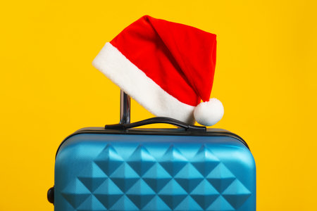 Blue suitcase with Santa hat on yellow backgroundの写真素材