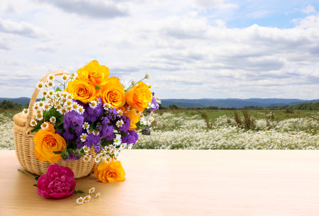 Beautiful flowers in wicker basket on table in blooming field. Space for textの写真素材